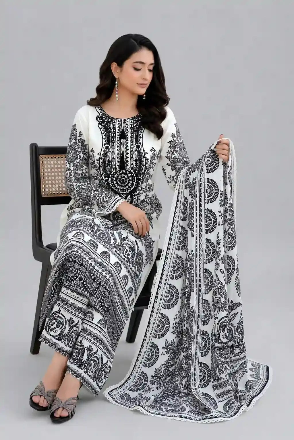 Woman sitting on a chair wearing a black and white Luxury lawn dress elegant design with same printed duppta and plain matching trouser