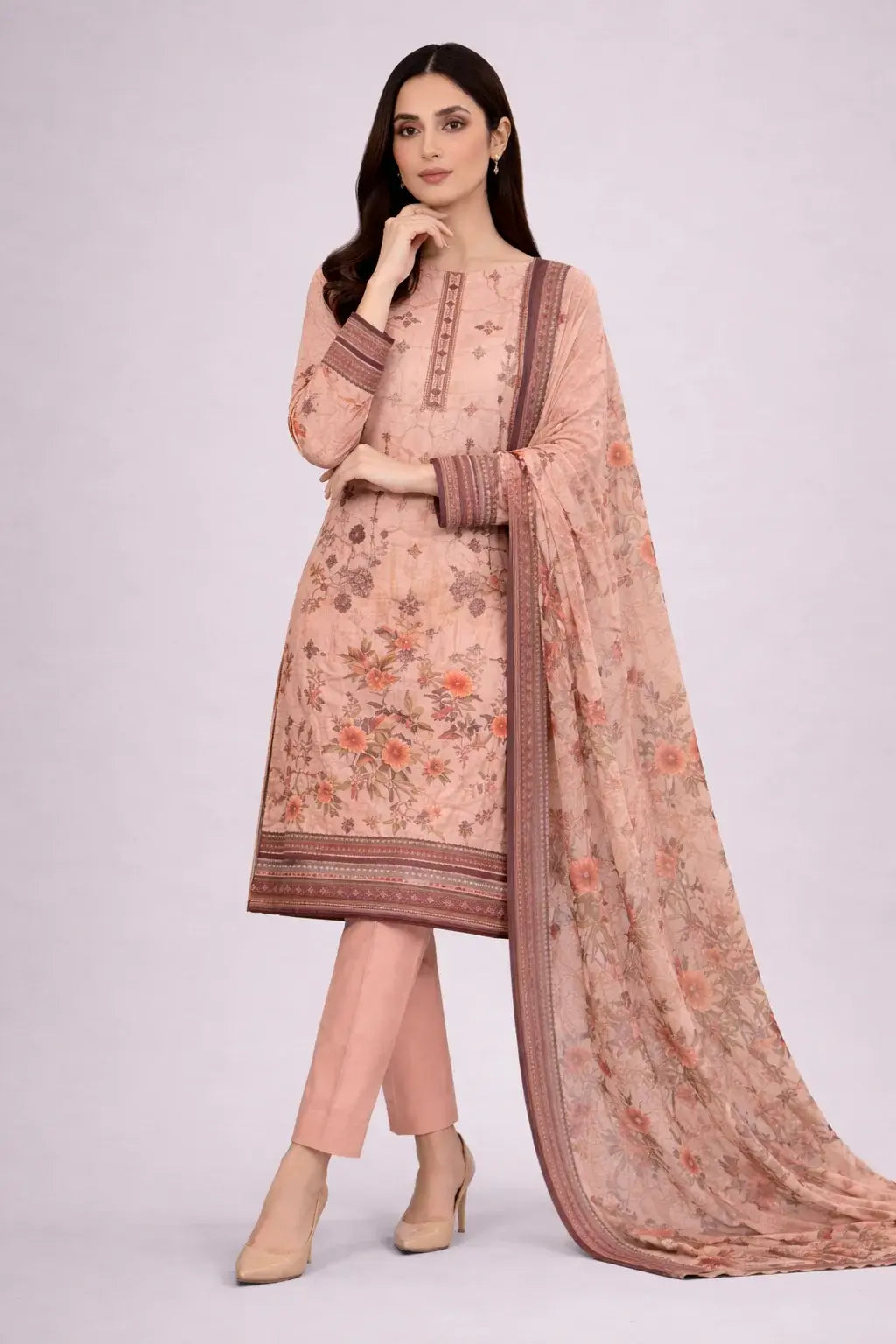 Woman wearing a peach-colored traditional lawn suite with a matching dupatta on a light gray background