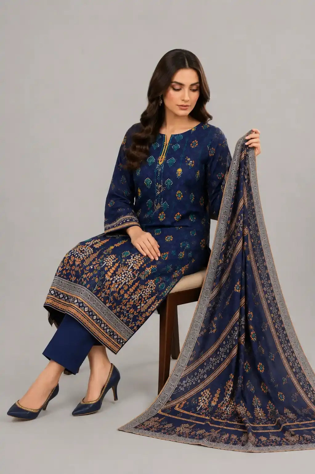 Woman in a blue embroidered outfit holding a matching dupatta on a gray background